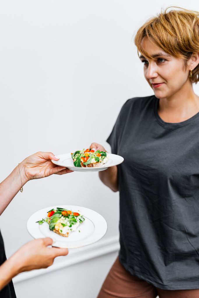 A woman in a gray shirt receiving a plate of healthy food indoors.